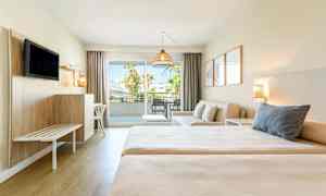 Et hotelværelse med to senge, en siddegruppe og balkon med udsigt. (AI-genereret tekst)