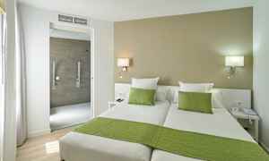 Hotelværelse med to enkeltsenge, grønt sengetøj og åbning til badeværelset. (AI-genereret tekst)