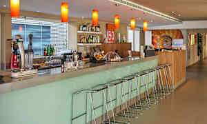 En moderne bar med barstole samt flasker og glas på hylder og borde. (AI-genereret tekst)