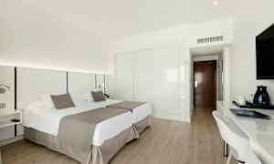 Et hotelværelse med to enkeltsenge, skrivebord og TV. (AI-genereret tekst)