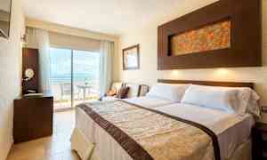 Et hotelværelse med dobbeltseng, skrivebord og altan med udsigt. (AI-genereret tekst)