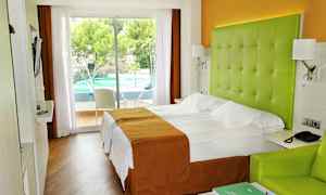 Hotelværelse med dobbeltseng, grøn sengegavl og udsigt til en udendørs swimmingpool. (AI-genereret tekst)