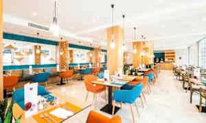 Billede af en moderne restaurant med farverige stole, træborde og dekorative lysarmaturer. (AI-genereret tekst)