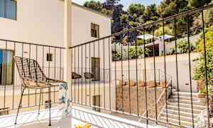 En altan med en stol og et gelænder, omgivet af en bygning og beplantning. (AI-genereret tekst)