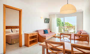 En hotelsuite med et bord, stole, sofa og et soveværelse synligt gennem en åben dør. (AI-genereret tekst)