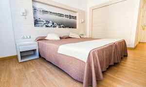 Hotelværelse med en stor seng med brunligt sengetæppe og hvidt sengetøj, trægulv og en vægdekoration i form af et sort-hvidt billede. (AI-genereret tekst)