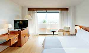 Et hotelværelse med to senge, et fjernsyn på en trækommode og en glasdør, der fører ud til en terrasse. (AI-genereret tekst)