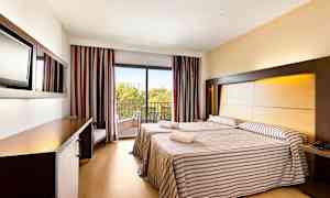 To senge i et hotelværelse med stribede tæpper, en balkon med udsigt og et arbejdsområde. (AI-genereret tekst)