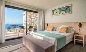 Hotelværelse med seng, siddepladser og udsigt til havet gennem store vinduer. (AI-genereret tekst)