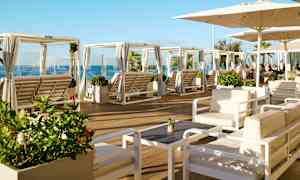 Loungeområde med siddegrupper og solsenge under parasoller samt havudsigt. (AI-genereret tekst)