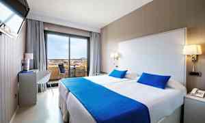 Et hotelværelse med en dobbeltseng, lyse vægge og blåt sengetøj. (AI-genereret tekst)