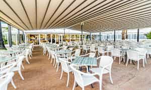 En udendørs restaurant med mange hvide borde og stole under et tag. (AI-genereret tekst)