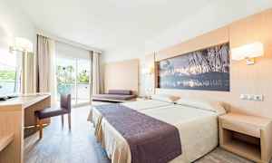 Et hotelværelse med en dobbeltseng, skrivebord, stol og en sofa. Værelset har en glasdør, der fører til en balkon. (AI-genereret tekst)