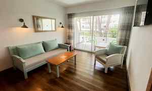 En siddegruppe med sofabord og stole samt et glasvindue, der fører ud til en altan. (AI-genereret tekst)