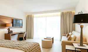 Billede af et lyst hotelværelse med seng, sofa og skrivebord. (AI-genereret tekst)