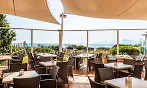 Billede af en udendørs terrasse med borde, stole og havudsigt. (AI-genereret tekst)