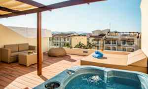 Terrasse med boblebad, sofa og udsigt over omkringliggende bygninger. (AI-genereret tekst)