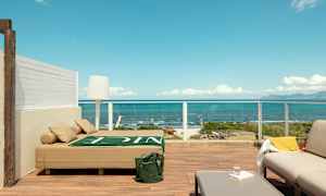 Terrasse med moderne møblering og udsigt over havet, inklusive en solseng, sofamøbler og bord. (AI-genereret tekst)