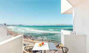 Udsigt fra en altan mod en strand med turkis vand, sand og personer, der bader. (AI-genereret tekst)