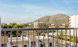 Udsigt fra en balkon over bygninger med tegltag og omkringliggende bylandskab, med et bjerg i baggrunden. (AI-genereret tekst)