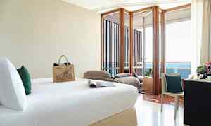 Et hotelværelse med en seng, skrivebord med stol og en altan med udsigt over havet. (AI-genereret tekst)