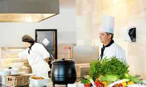 To kokke ved en serveringsstation med grøntsager og mad. (AI-genereret tekst)