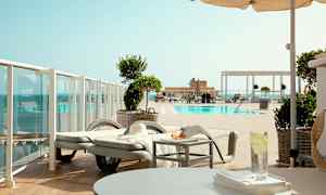 Udsigt over en pool med liggestole og parasoller. (AI-genereret tekst)