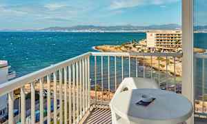 Udsigt fra en balkon mod en kyst med hav og bygninger i baggrunden. (AI-genereret tekst)