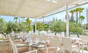 Restaurant med hvide møbler og tag, omgivet af grønt. (AI-genereret tekst)