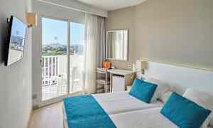 Et lyst hotelværelse med to senge, blå puder og sengetæpper samt en balkon med udsigt. (AI-genereret tekst)