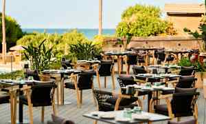 Udendørs restaurant med borde og stole samt grønne planter. (AI-genereret tekst)