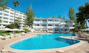 En udendørs pool med liggestole og parasoller foran en hvid bygning, omgivet af træer. (AI-genereret tekst)