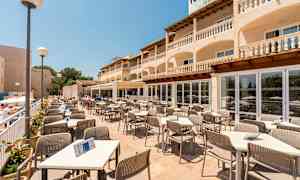 Terrasserestaurant med borde og stole, omgivet af en bygning med altaner. (AI-genereret tekst)