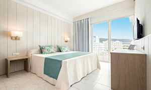 Et lyst hotelværelse med en dobbeltseng med hvidt og turkis sengetøj, to natborde, et klædeskab og en balkon med udsigt over byen. (AI-genereret tekst)