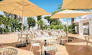 Billede af en terrasse med borde, stole og parasoller i en solrig atmosfære. I baggrunden er der liggestole og grønne områder. (AI-genereret tekst)