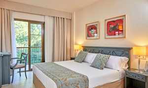 Et hotelværelse med en dobbeltseng, natborde, to bordlamper og en stol ved et skrivebord. Bag sengen hænger to billeder på væggen. (AI-genereret tekst)