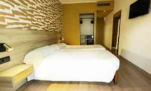 Et hotelværelse med to enkeltsenge, et vægmonteret fjernsyn og et garderobeskab. (AI-genereret tekst)