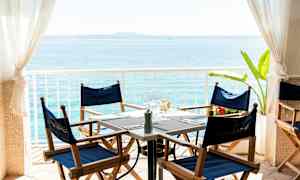 Udsigt over et opdækket bord med blå stole og hav i baggrunden. (AI-genereret tekst)