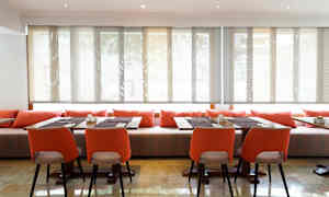 Et rum med borde og stole, dekoreret med orange puder og solafskærmede vinduer. (AI-genereret tekst)