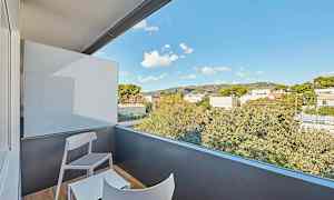 En altan med to stole og et bord, med udsigt over omkringliggende træer og bygninger under en blå himmel. (AI-genereret tekst)