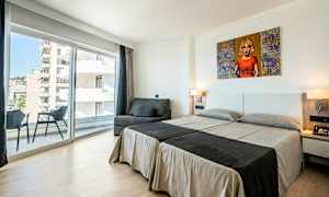 Et hotelværelse med to enkeltsenge, en sofa, en balkon og store glasvinduer. (AI-genereret tekst)