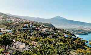 En udsigt over et kuperet landskab med huse og vegetation samt en bjergtop i baggrunden. (AI-genereret tekst)