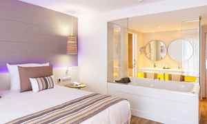 Hotelværelse med en seng og et indbygget badekar, der vender mod et badeværelse. (AI-genereret tekst)