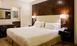 Et hotelværelse med en stor seng, to senge lamper, et natbord og en telefon. En åbning til et badeværelse ses i baggrunden. (AI-genereret tekst)