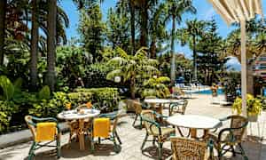 Udendørs serveringsområde med borde og stole nær en pool og frodig vegetation. (AI-genereret tekst)