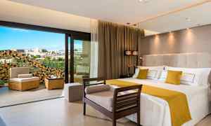 Et moderne hotelværelse med en stor seng og siddepladser samt en åbning til en balkon med udsigt. (AI-genereret tekst)