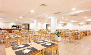 En spisesal med træborde og stole. Rummet er lyst og rummeligt med servietter og opsatte glas. (AI-genereret tekst)