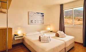 Et lyst hotelværelse med en dobbeltseng, vindue med udsigt over landskabet og et vægmaleri over sengen. (AI-genereret tekst)