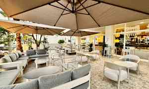 Udendørs serveringsområde med sofaer og borde under parasoller. (AI-genereret tekst)