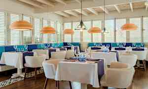 En elegant restaurant med hvide duge, blå dekoration og moderne loftslamper. (AI-genereret tekst)